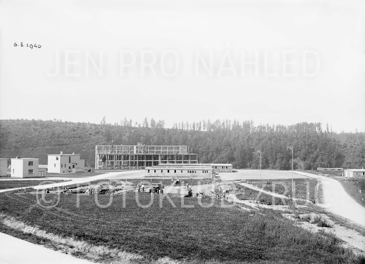 Příprava stavby společenského domu: v pozadí tovární budovy, dřevěné ubikace a vila vedoucího závodu na fotografii z 6. 8. 1940 (Fotoklub Zruč nad Sázavou).